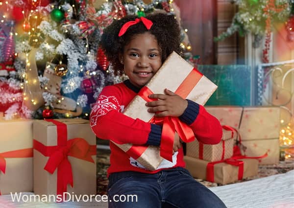 Little girl by Christmas tree hugging a gift Little girl by Christmas tree hugging a gift